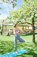 Outdoor portrait of happy young pregnant woman practicing youga in spring garden under blooming apple trees, healthy lifestyle photo