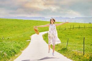 Outdoor portrait of young pregnant woman walking in countryside between green pasture fields, arms wide open, healthy and happy expecting woman photo