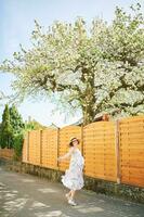 Outdoor maternity portrait of happy young pregnant woman standing next to blooming tree, springtime photo