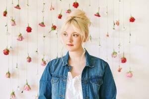 Studio portrait of pretty young teenage 15 - 16 year old girl wearing denim jacket, posing on white background with hanging flowers, beauty and fashion concept photo