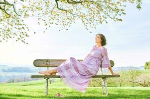 Outdoor portrait of happy pregnant woman enjoying nice sunny day in spring garden photo