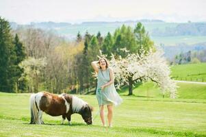 Outdoor portrait of happy young woman playing with pony, farm vacation photo