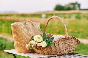 Romantic outdoor image of straw bag and basket full of freshly cut roses photo