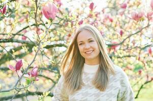 Outdoor portrait of beautiful happy model with blond hair posing next to magnolia flowers photo