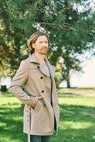 Outdoor portrait of handsome young man with red hair, wearing beige coat photo