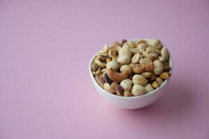 f many mixed nuts in white bowl on light pink background photo