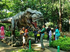 Bandung ciudad, Oeste Java, Indonesia. 19 octubre 2023. realista modelo de dinosaurio tiranosaurio rex en fuera puerta parque. familia reunión con lleno de divertido y felicidad foto