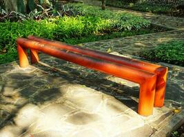 Lonely bench in the public city park. Red rusty metal bench in the park during summer day. An empty iron park bench at the edge of a path. photo