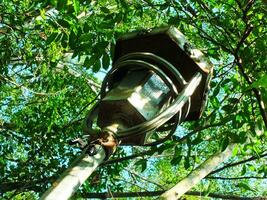 Old and broken street lamp in the park. Abandoned old lamp with lush green leaf background photo