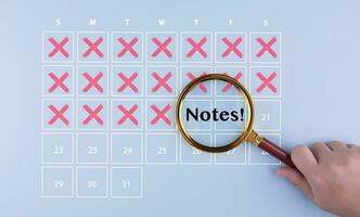 Handhold the Magnifying glass focus schedule calendar in the agenda reminder and Vacation travel in the calendar reminder event concept. The red cross marked with pen on a calendar sheet, photo