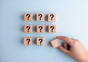 Hand holds Wooden cube block light bulb icon and question mark, a column of wooden blocks with question sign mark. copy space, FAQ frequently asked questions, Answers and Information photo