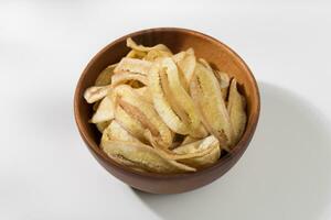 Banana chips in a wooden bowl on a white table photo