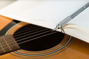 A brown pencil and a dark red notebook are placed on an acoustic guitar. photo