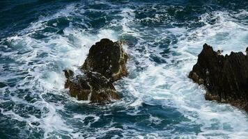 uma mar onda bate em a pedras com grande salpicos, visto a partir de acima dentro super lento movimento video