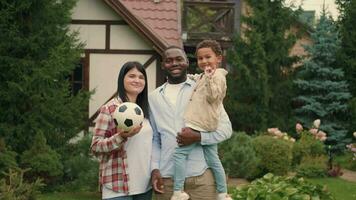 Portrait Cheerful family playing football near the house on the lawn.African dad,Caucasian mom, son. video