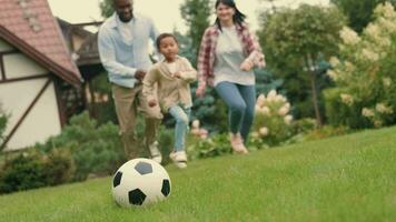 A cheerful family is playing football near the house on the lawn. African dad, Caucasian mom, son. video