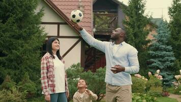 Portrait Cheerful family playing football near the house on the lawn.African dad,Caucasian mom, son. video