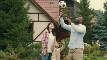retrato alegre família jogando futebol perto a casa em a gramado.africano pai, caucasiano mãe, filho. video