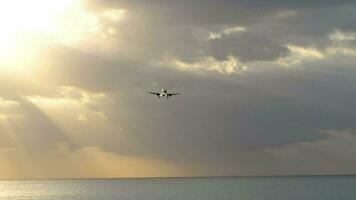 Panoramic view of the silhouette of an aircraft landing with extended landing gear, sky with different types of clouds gradient illuminated by the evening sun leaving the horizon video