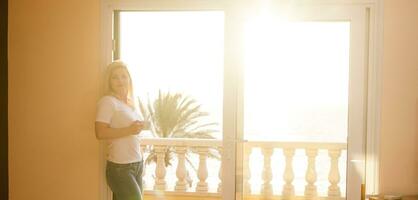 mujer cerca ventana frente a el amanecer a Mañana foto