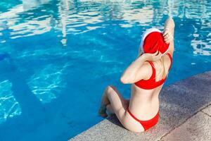 Beautiful young woman in Santa hat near swimming pool photo