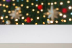 An empty white wooden table in front of a blurry Christmas tree background. Photo
