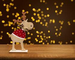 A wooden Christmas deer stands on a wooden table, blurry bokeh background. Blurred light gold bokeh. photo