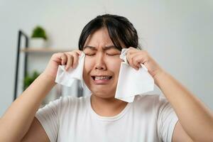 retrato de un triste asiático mujer llorando toallitas su lágrimas con un pañuelo de papel papel toalla. foto