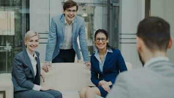 Team of cheerful business colleagues talking and discussing each other while having break sitting on sofa in modern office hall indoors photo