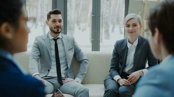 Cheerful businessman and businesswoman talking and duscussing future contract with business partners sitting on couch in meeting room indoors photo