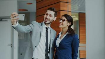 Happy businessman and his female colleague taking a selfie on smarphone camera for social media in modern office indoors photo