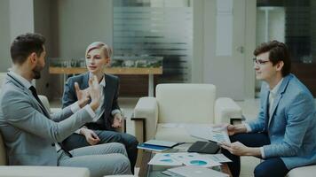 businessman discussing financial reports with female and male business partners sitting on sofa in modern office hall with indoors photo