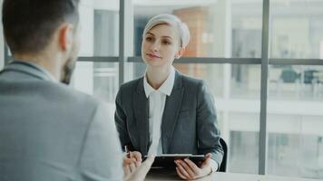 hora mujer de negocios teniendo trabajo entrevista con joven hombre en traje y acecho su currículum solicitud en moderno oficina adentro foto