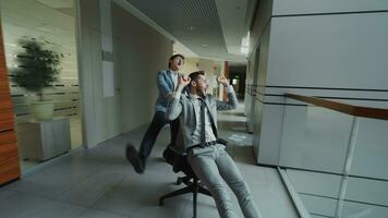 Two crazy businessmen riding office chair and throwing papers up while having fun in lobby of modern business center indoors photo