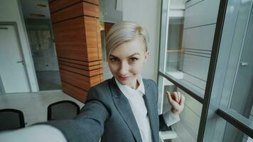 POV of young businesswoman in suit taking a selfie photo holding smartphone and have fun in modern office indoors