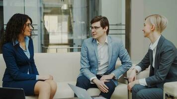 Businessman talking and duscussing future contract with female business partners sitting on couch in meeting room indoors photo