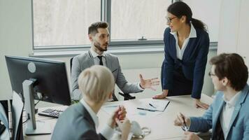 Young businessman talking with male and female colleagues sitting at the table in modern office indoors photo