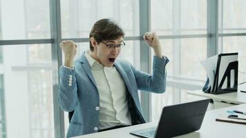 Young businessman using laptop computer receiving good message and become very excited and happy sitting in modern office indoors photo