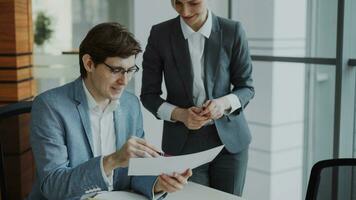 Two business colleagues discussing reports in modern office indoors. Businessman sitting at the table talking his female partner photo