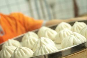 chino alimento, baozi es un tradicional delicadeza en porcelana, un pan comida fotografía entonces tentador, delicioso baozi, chino al vapor carne bollo es Listo a comer en servicio plato y buque de vapor foto