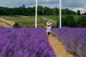 joven mujer en blanco vestir en un columpio disfrutando el belleza y fragancia de un archivado de lavanda en floración. alto calidad foto. foto