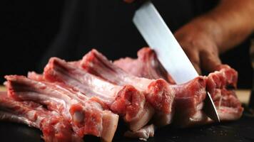 The chef cuts raw meat, BBQ ribs with a knife. Raw beef sliced on a wooden board. Delicious food concept photo