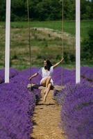 Young woman in white dress on a swing enjoying the beauty and fragrance of a filed of lavender in bloom. Lavender field summer sunset landscape near Valensole. Provence, France. photo