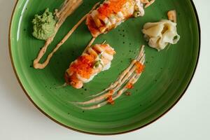 Sushi nigiri with a grilled salmon and caviar. Sushi rolls on green plate with wasabi and ginger. Top view with copy space. Traditional japanese dish. photo