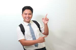 Indonesian senior high school student wearing white shirt uniform with gray tie showing product, pointing at something and smiling. Isolated image on white background photo