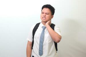 Indonesian senior high school student wearing white shirt uniform with gray tie touching his neck and expressing negativity. Isolated image on white background photo