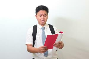 Indonesian senior high school student wearing white shirt uniform with gray tie reading journal report with upset expression. Isolated image on white background photo