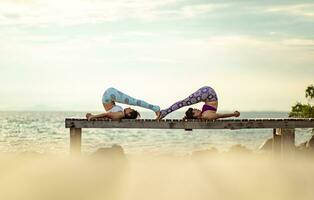 couples of woman playing yoga pose on beach pier with moring sun light photo