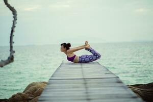 beautiful woman playing yoga in turtle pose on sea wooden pier photo