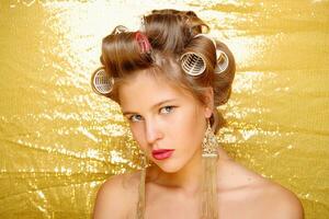 Beautiful girl in hair curlers isolated on gold photo